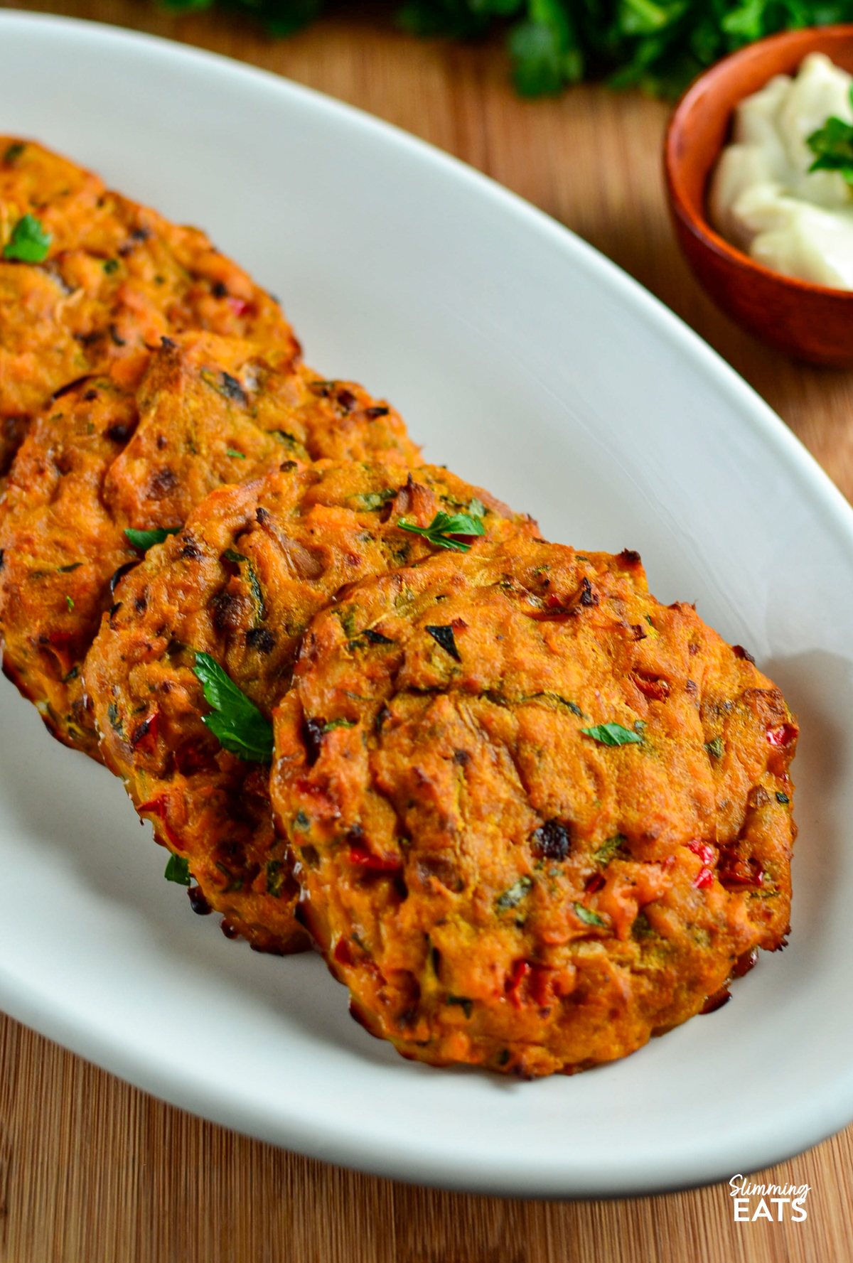 just baked Oven Baked Tuna Sweet Potato Patties on a white oval plate scattered with fresh parsley, small wooden bowl with mayo on the side