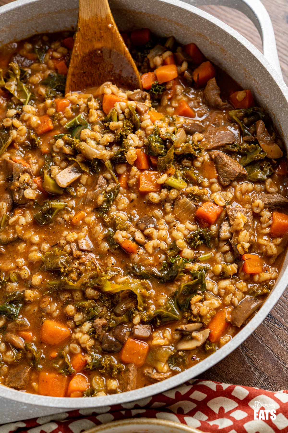 Beef and barley stew in casserole pot with wooden spoon