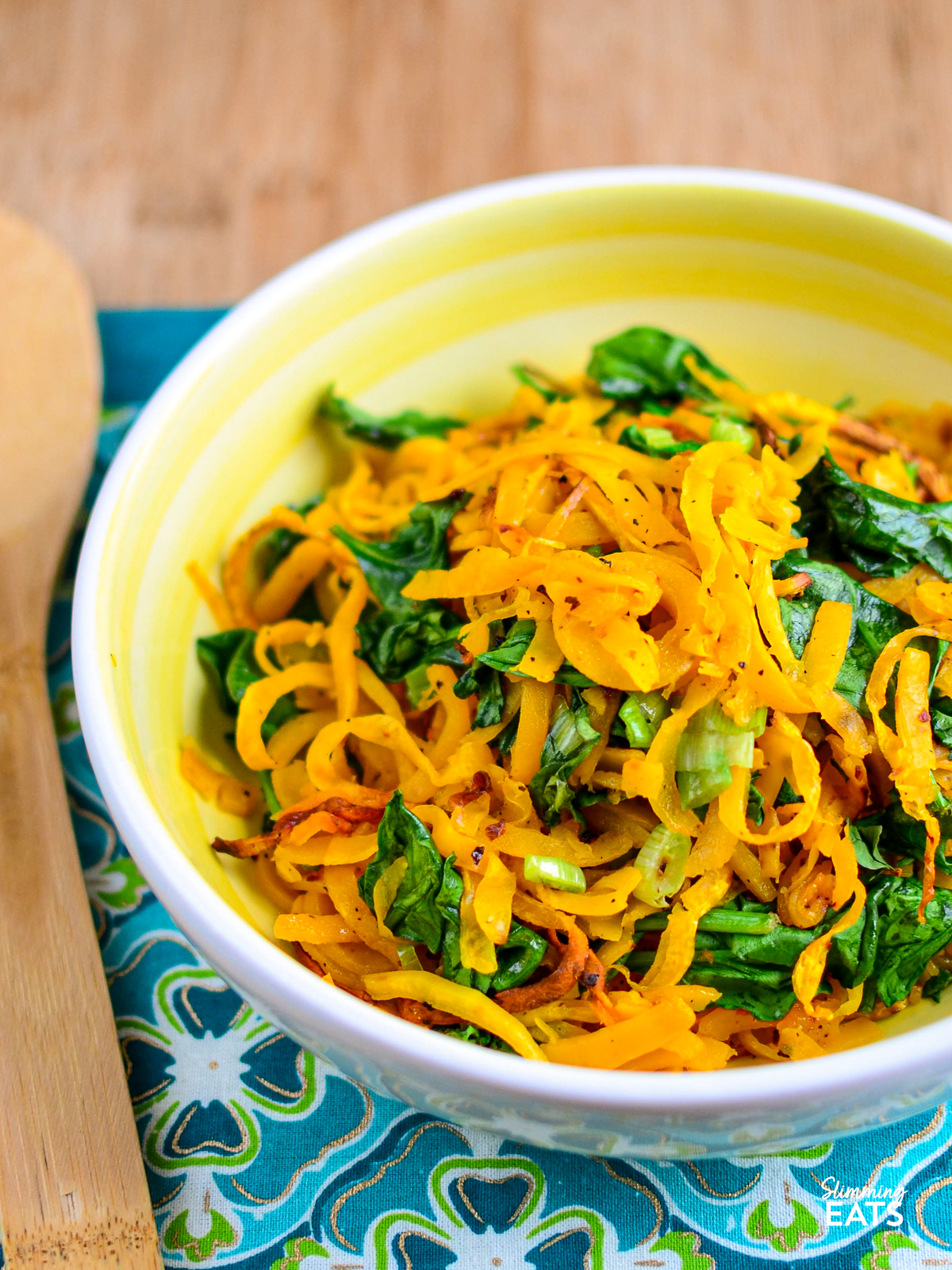 oven baked butternut squash noodles in a yellow and white bowl with spinach and spring onions