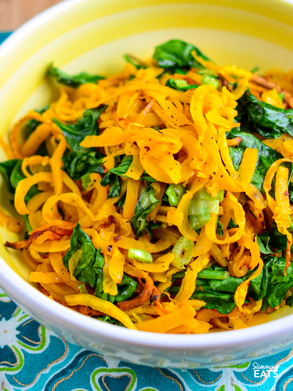 oven baked butternut squash noodles in a yellow and white bowl with spinach and spring onions