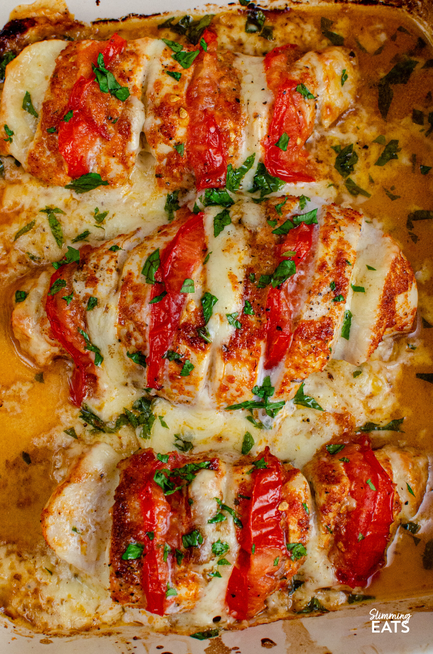 This Tomato Mozzarella Hasselback Chicken turns simple chicken breasts into an easy family dinner with juicy tomato and melted mozzarella. close up of Three tomato and mozzarella stuffed hasselback chicken in a ceramic baking dish