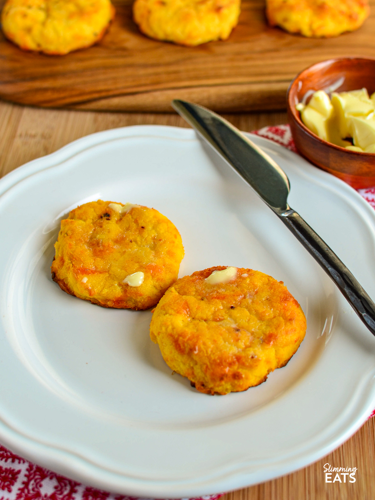 two sweet potato cheddar scones on white plate with knife and spread with butter