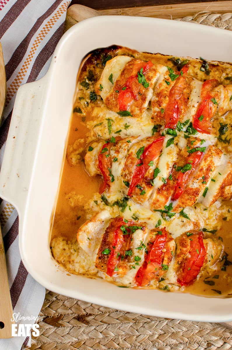 Cheesy goodness of Tomato and Mozzarella Hasselback Chicken - this is one chicken dish you just have to try. Gluten Free,Slimming and Weight Watchers friendly tomato and mozzarella hasselback chicken in oven proof dish on placemat