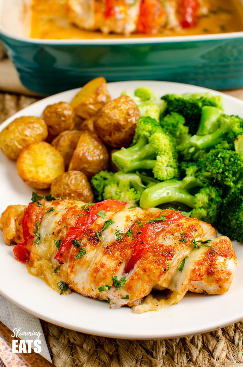 tomato and mozzarella hasselback chicken on white plate with golden potatoes and broccoli