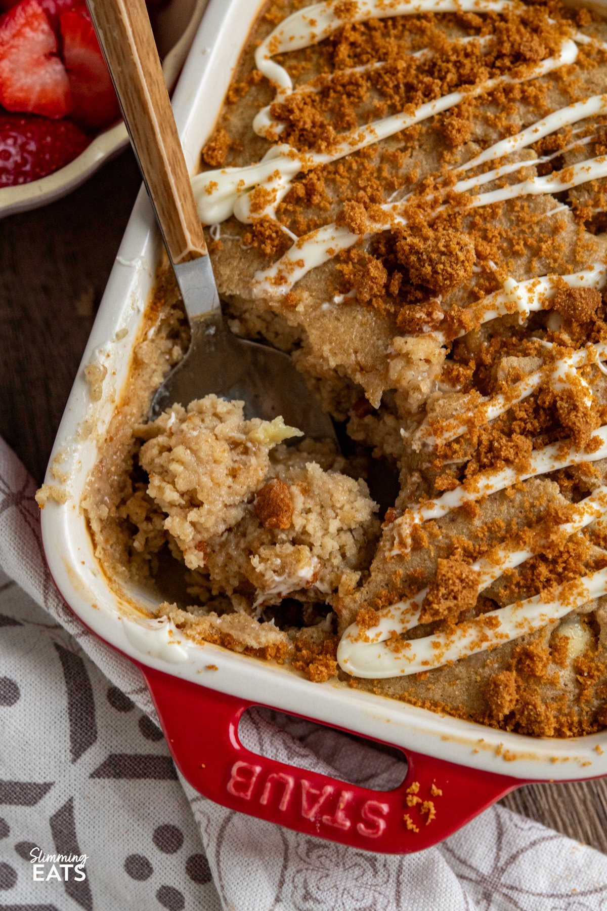 close up of spoon in White Chocolate Chip Oatmeal Cake with Biscoff Cookie Crumb in red mini staub baking dish 
