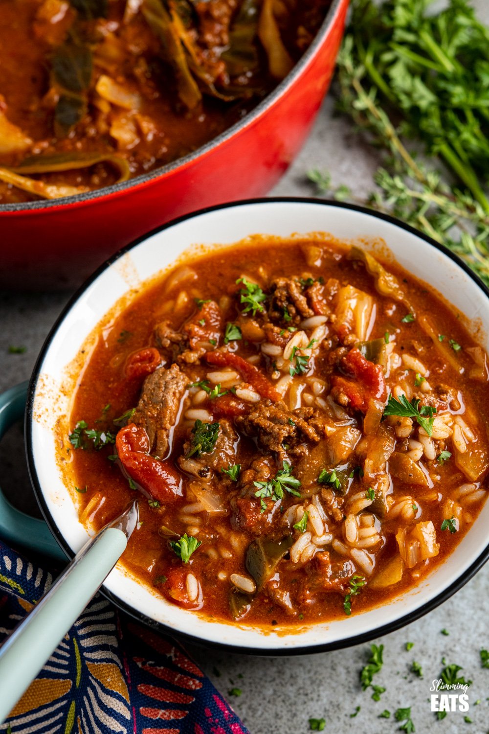 blue grey soup bowl filled with beef and cabbage soup and added rice, herbs in background