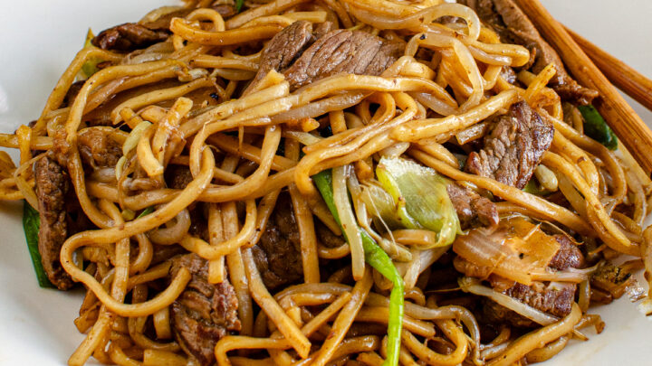 beef chow mein on a white plate with chopsticks on the right