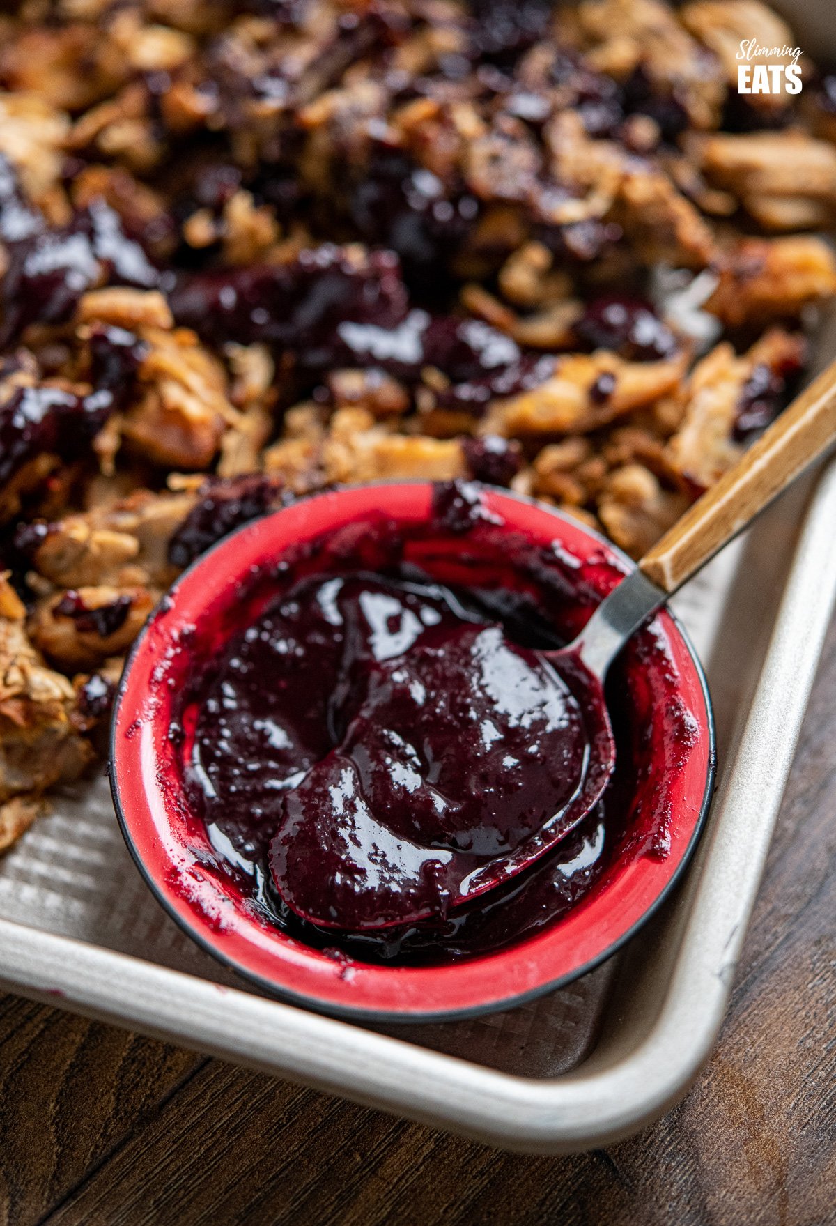 blueberry bbq sauce in small red bowl with a spoon on baking tray with pulled pork