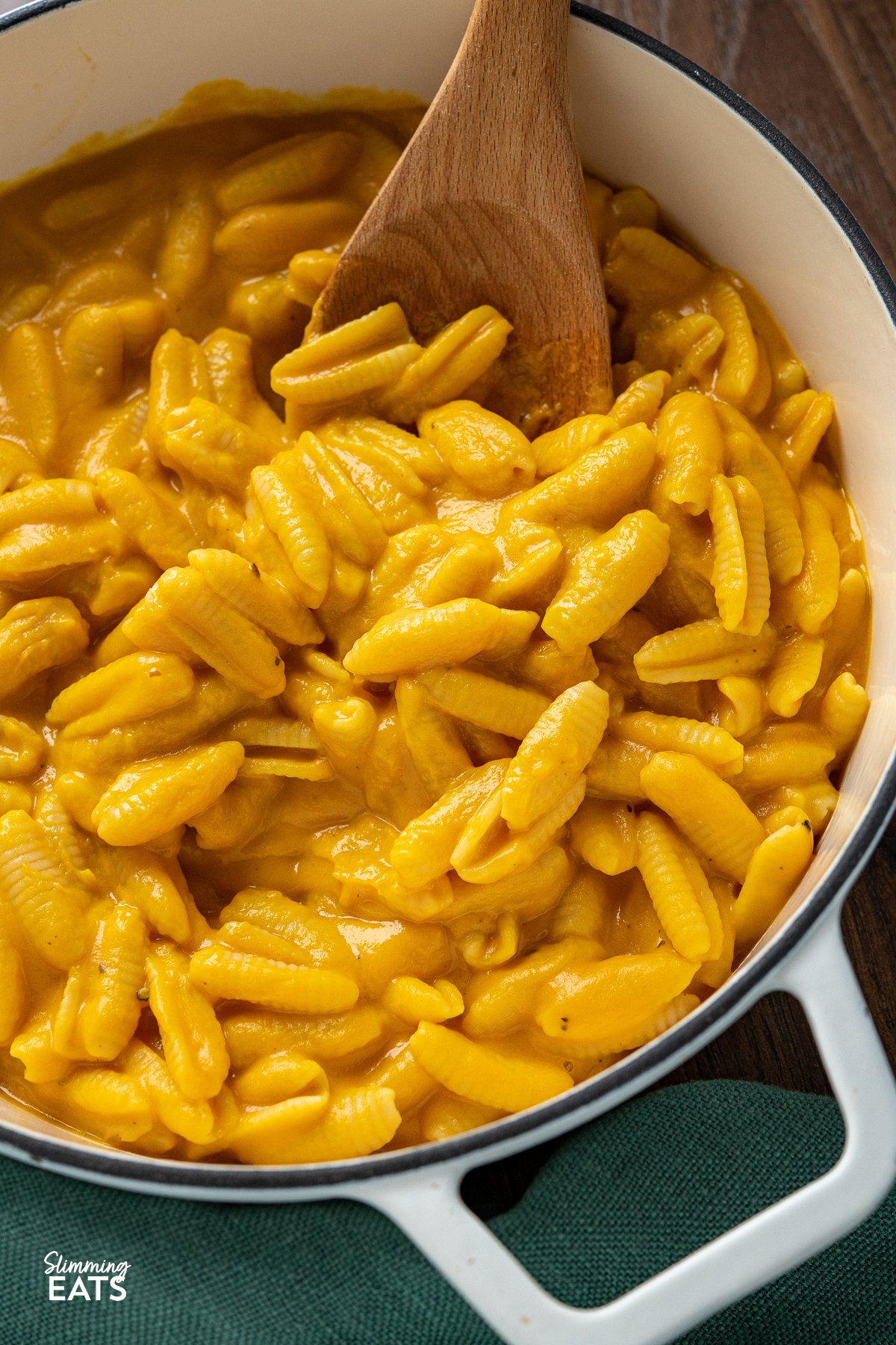 Savour the delightful flavors of a comforting bowl of creamy mac and cheese, elevated with the incorporation of pureed butternut squash for a lighter calorie count. This clever twist preserves the ideal balance of rich cheesiness and velvety creaminess, making every bite a truly satisfying treat. close up Creamy Butternut Squash Mac and Cheese in a white cast iron pan with two handles