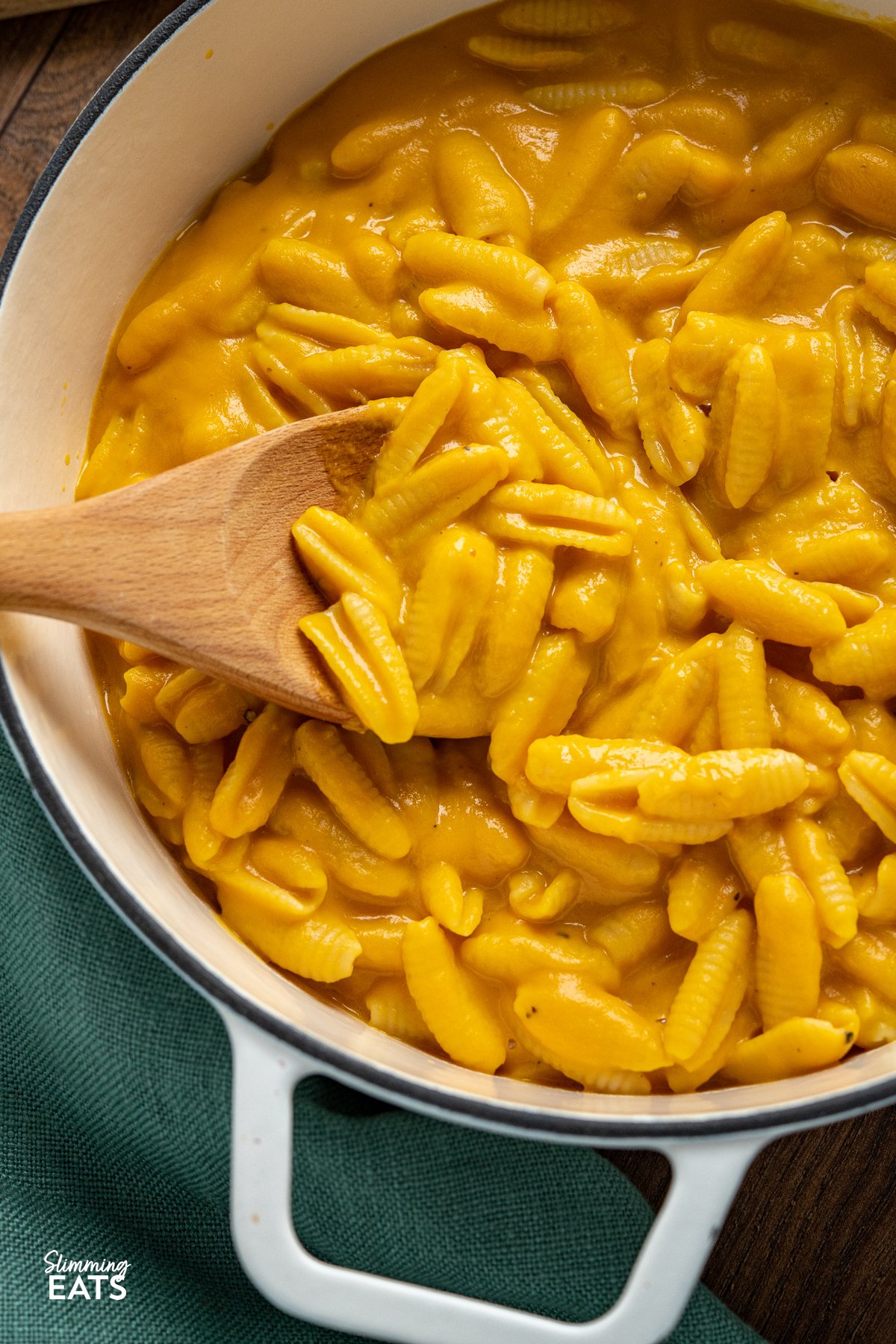 Savour the delightful flavors of a comforting bowl of creamy mac and cheese, elevated with the incorporation of pureed butternut squash for a lighter calorie count. This clever twist preserves the ideal balance of rich cheesiness and velvety creaminess, making every bite a truly satisfying treat. close up of Creamy Butternut Squash Mac and Cheese in a white cast iron pan with two handles