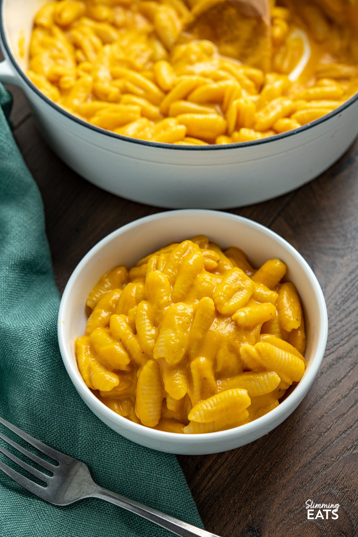 Creamy Butternut Squash Mac and Cheese in a white bowl on wooden board, white cast iron pan in background