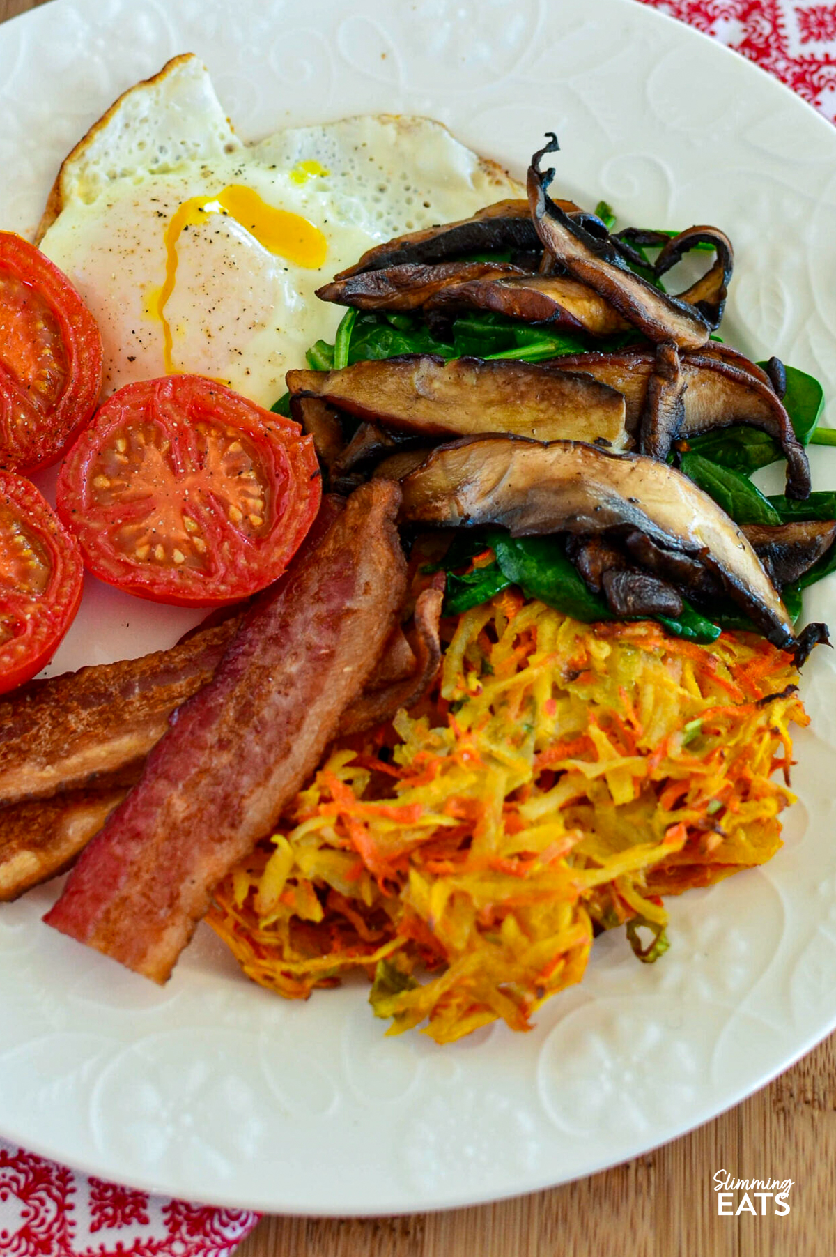 carrot, parsnip and potato hash on a white plate with bacon, egg, tomatoes, mushrooms and spinach