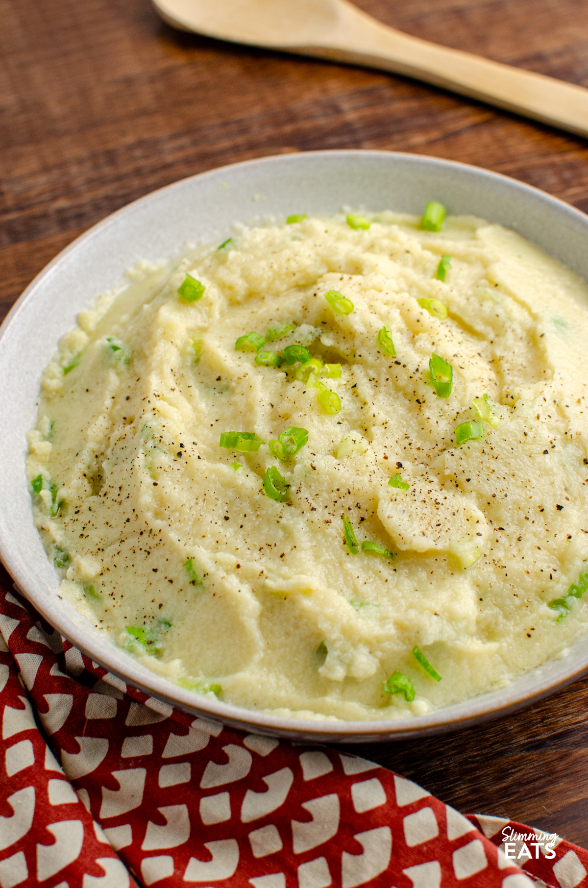 Sour Cream and Spring Onion Cauliflower Mash in a bowl on a wood board with wooden spoon