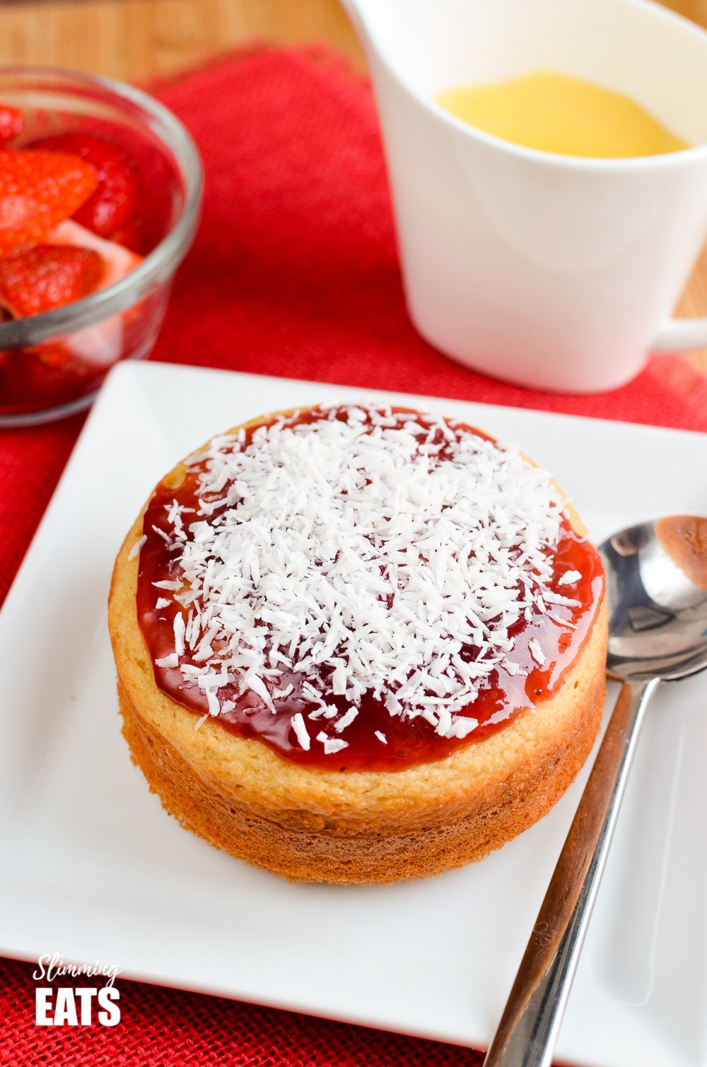 Jam and Coconut Sponge Cake - a delicious journey back to childhood with this oat based coconut sponge, topped with sweet jam and shredded coconut. A perfect filling start to your day. Gluten Free, Vegetarian, Slimming and Weight Watchers friendly jam and coconut sponge cake on a white plate with spoon.
