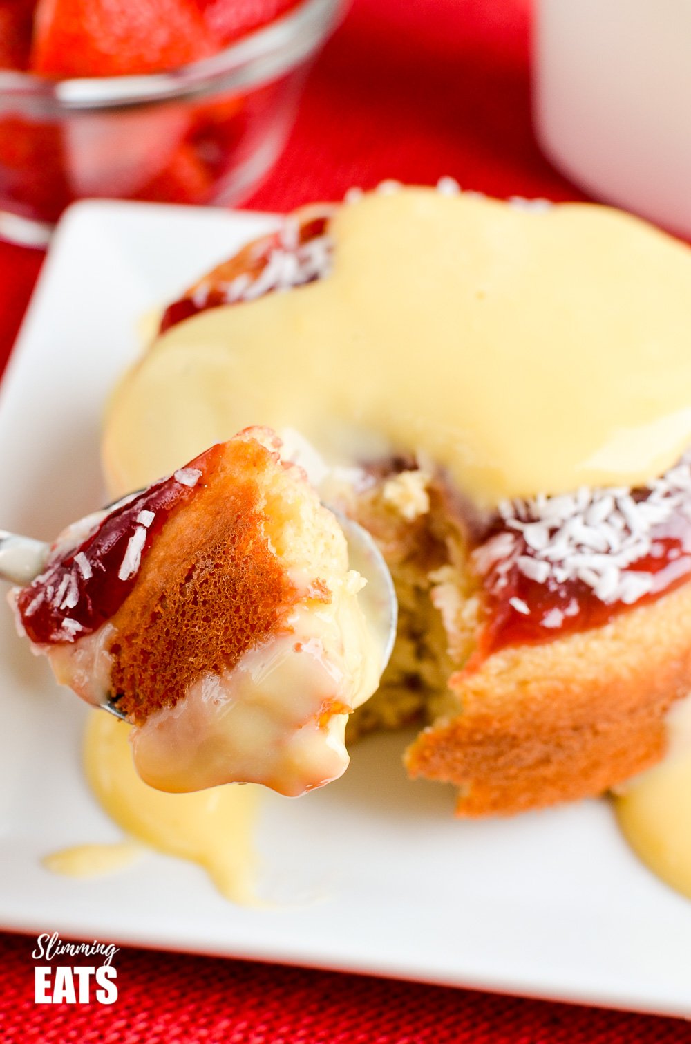 Jam and Coconut Sponge Cake - a delicious journey back to childhood with this oat based coconut sponge, topped with sweet jam and shredded coconut. A perfect filling start to your day. Gluten Free, Vegetarian, Slimming and Weight Watchers friendly spoon of jam and coconut sponge cake from white plate