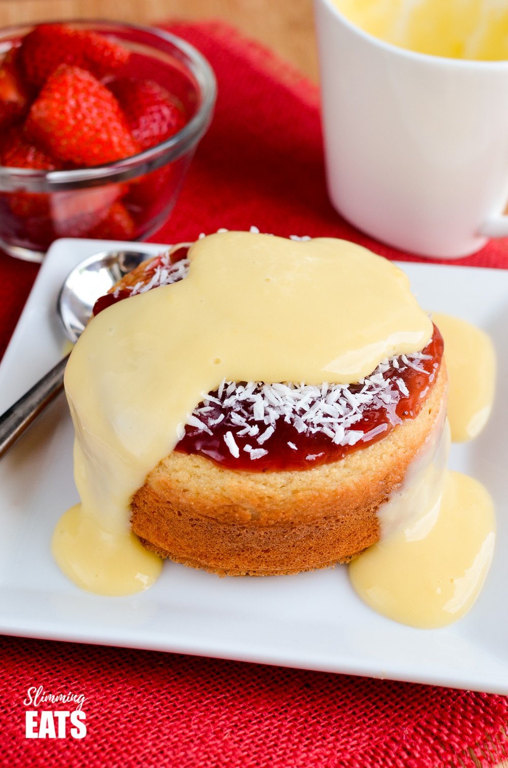 Jam and Coconut Sponge Cake - a delicious journey back to childhood with this oat based coconut sponge, topped with sweet jam and shredded coconut. A perfect filling start to your day. Gluten Free, Vegetarian, Slimming and Weight Watchers friendly custard over jam and coconut sponge cake on white plate