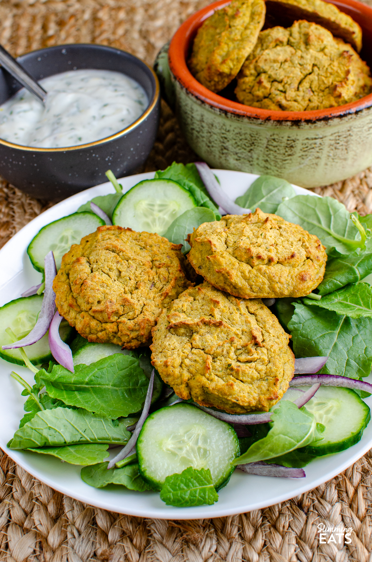 oven baked falafel on a bed of salad on a white plate, dip and ceramic dish with remaining falafel in background