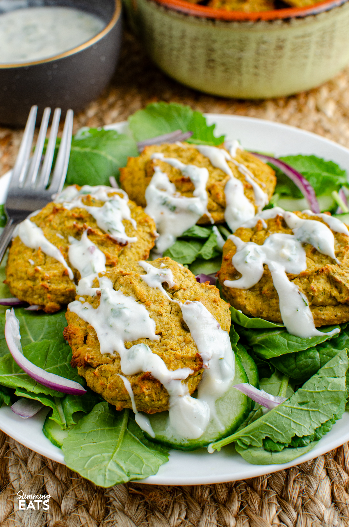 close up of oven baked falafel on a bed of salad on a white plate, drizzled with yoghurt dip