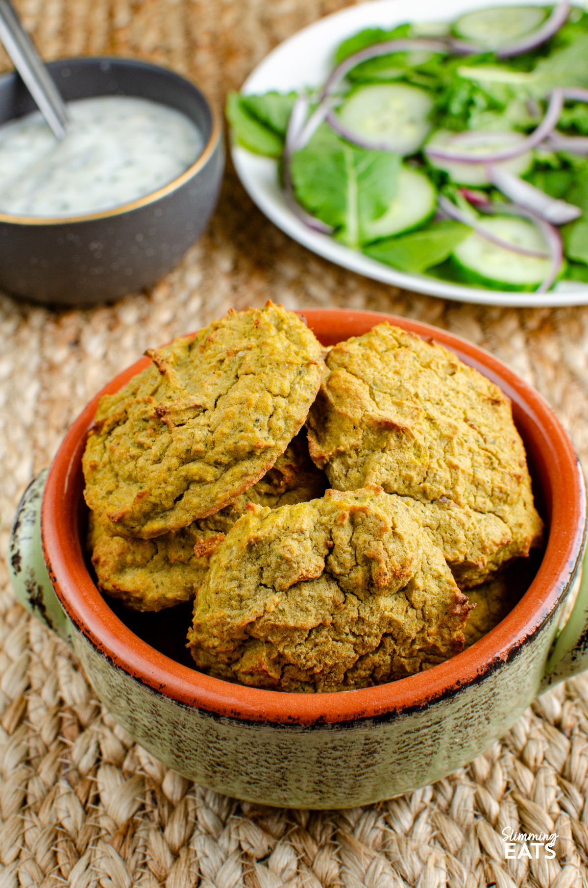 oven baked falafel in a light green ceramic dish, dip and salad in background