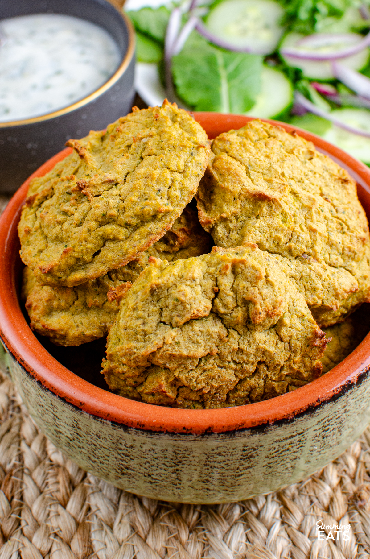 close up of oven baked falafel in a light green ceramic dish, dip and salad in background
