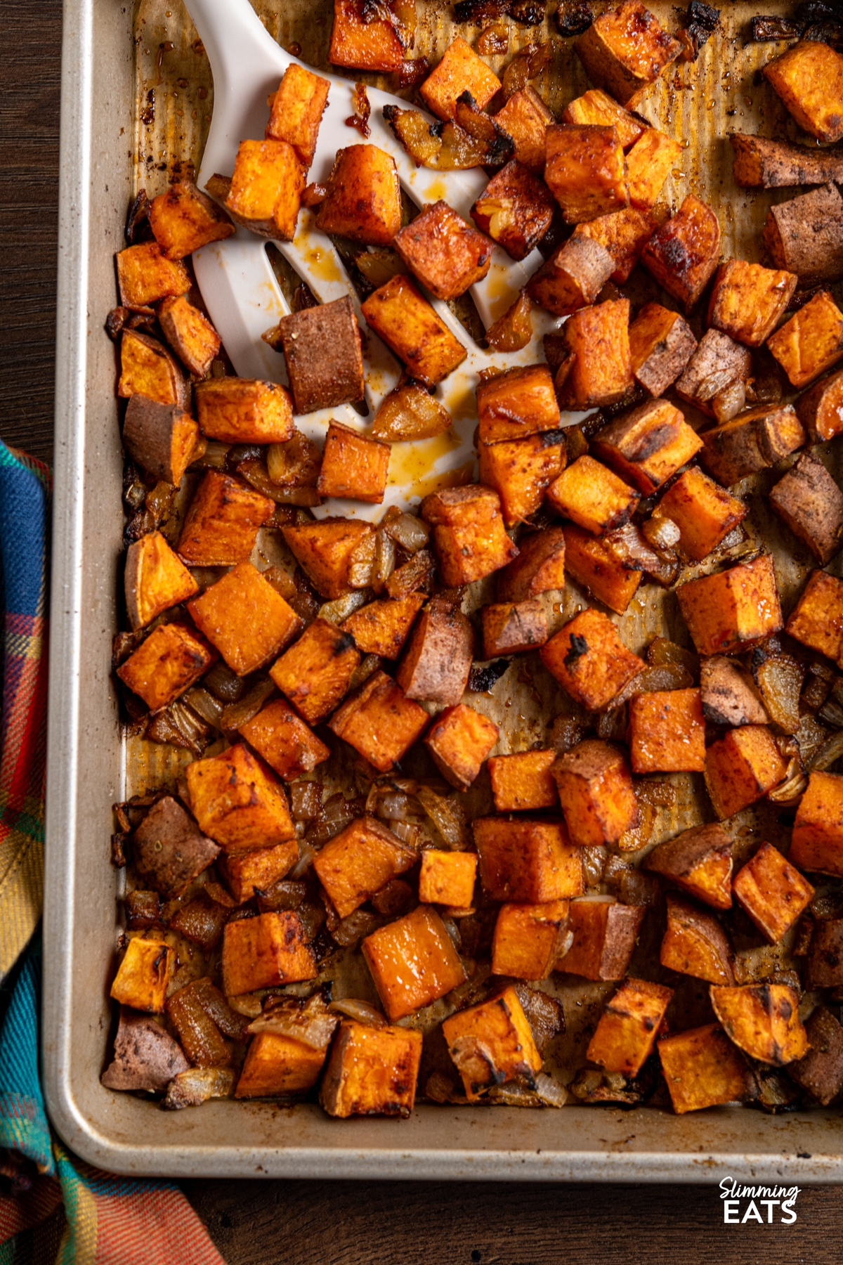 roasted skin on seasoned sweet potato cubes with onion on a parchment lined baking tray