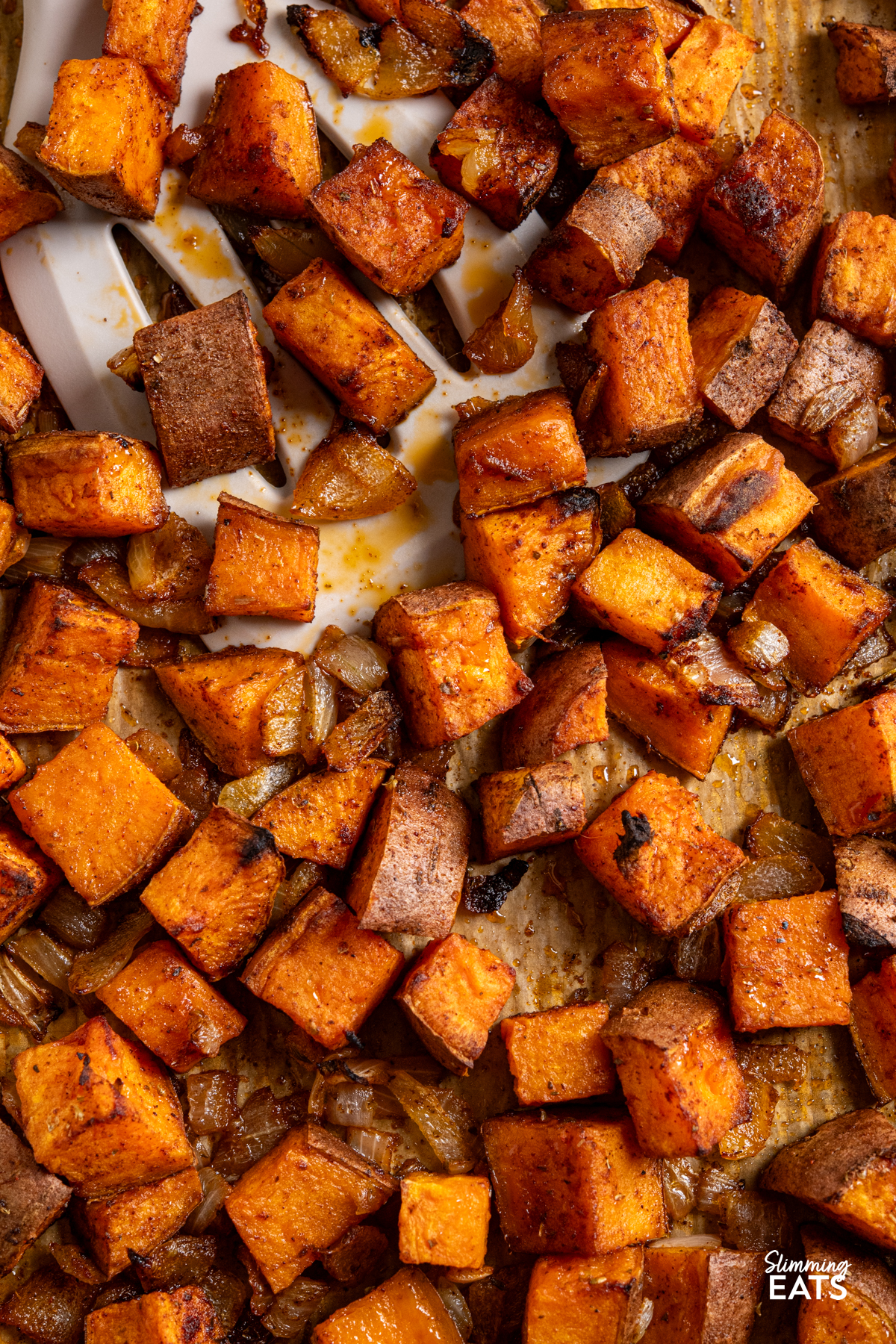 close up of roasted skin on seasoned sweet potato cubes with onion on a parchment lined baking tray