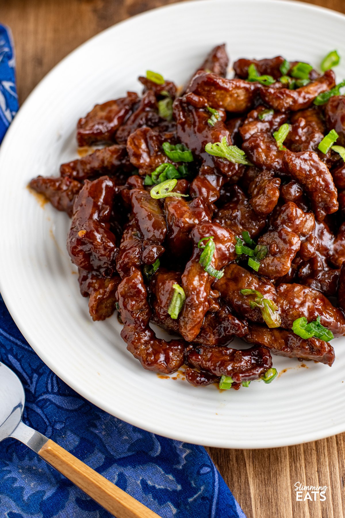 close up of Sweet Chilli Beef on a white plate, sprinkled with spring onions