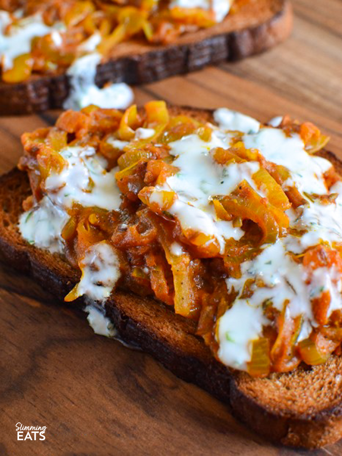 close up of Onion Masala Toast on a wooden board drizzled with mint yoghurt