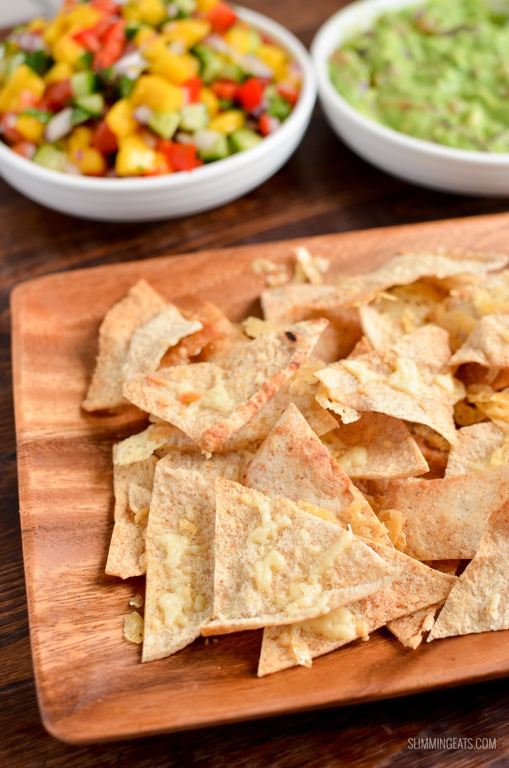 cheddar pita chips on a wooden plate with mango Salsa and guacamole