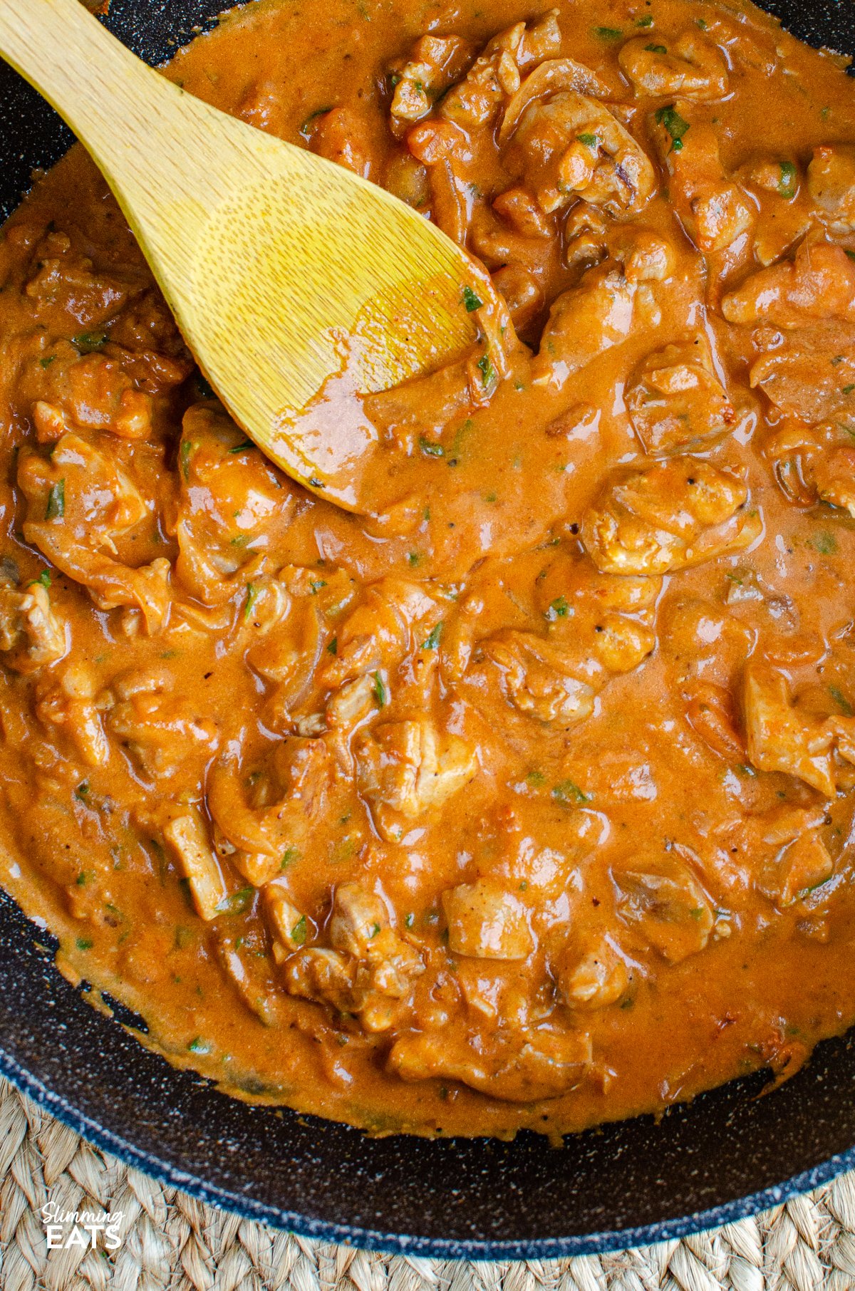 creamy chicken and tomatoes in a non stick frying pan with a wooden spoon placed in pan