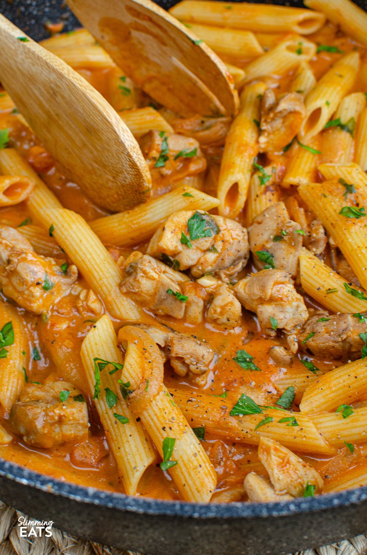 creamy chicken and tomatoes in a frying pan with cooked pasta, sprinkled with parsley