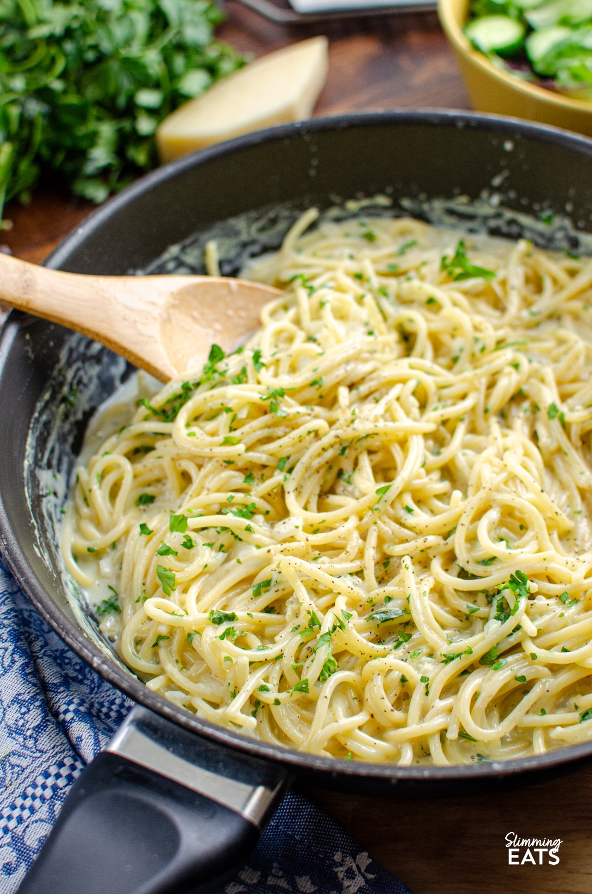 Tuck into a bowl of this irresistibly creamy garlic pasta — a quick, fuss-free one-pot dish that’s perfect for busy evenings. Made with simple, everyday ingredients and ready in under 20 minutes, it’s the kind of comforting meal the whole family will happily dive into. Creamy Garlic Pasta in a deep frying pan with wooden spoon, surrounded by components of the recipe