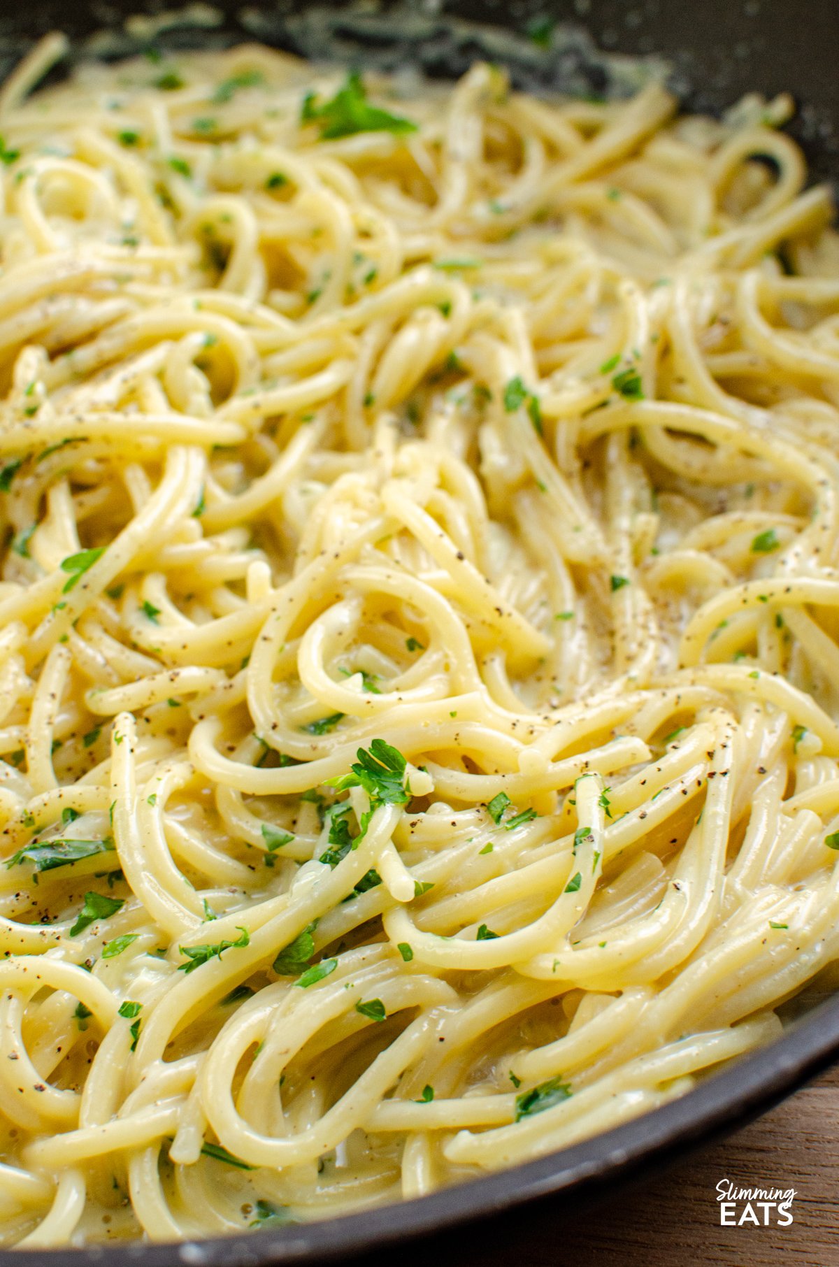Tuck into a bowl of this irresistibly creamy garlic pasta — a quick, fuss-free one-pot dish that’s perfect for busy evenings. Made with simple, everyday ingredients and ready in under 20 minutes, it’s the kind of comforting meal the whole family will happily dive into. close up of Creamy Garlic Pasta in a deep frying pan with wooden spoon