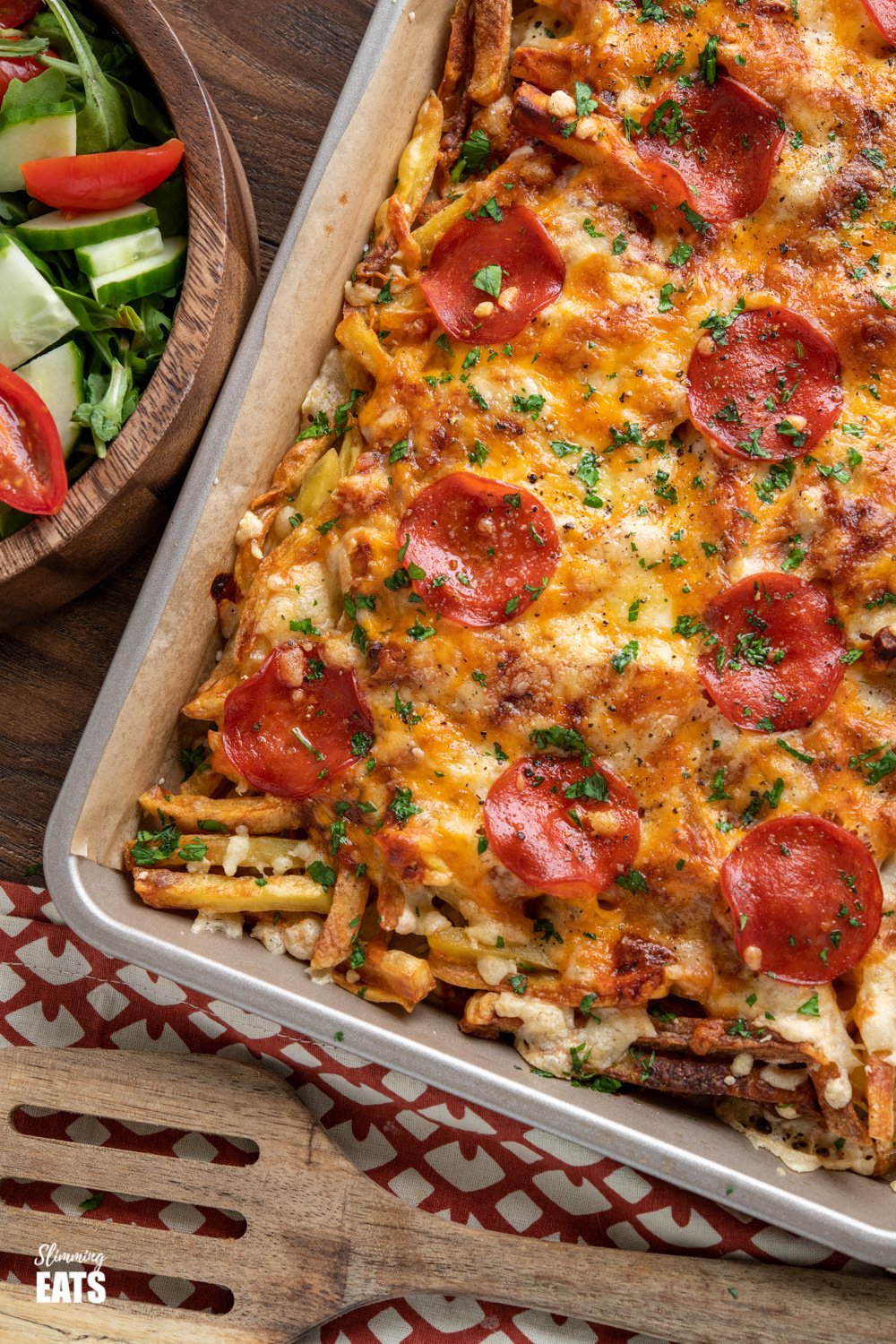 close up of Cheesy Oven Baked Pizza Fries with wooden bowl of salad to the left