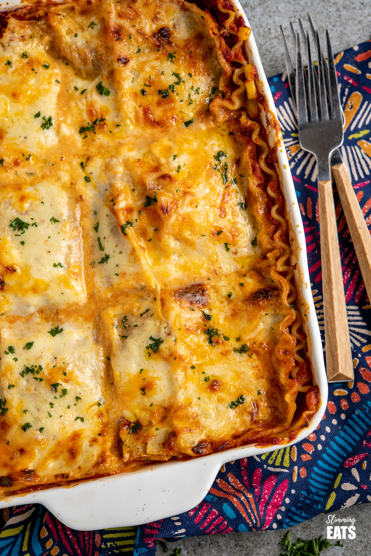 Chicken and sweetcorn Lasagne - A family favourite, tender pieces of chicken breast and sweetcorn in a veggie packed pasta sauce all topped with a delicious lighter béchamel sauce and cheese. #weightwatchers close up of chicken and sweetcorn lasagne in a white oven proof dish with two forks placed to the right