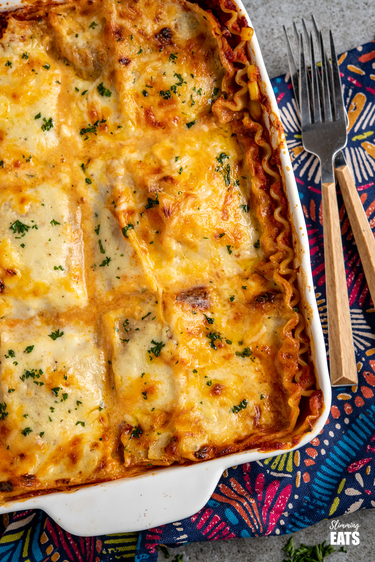 close up of chicken and sweetcorn lasagne in a white oven proof dish with two forks placed to the right