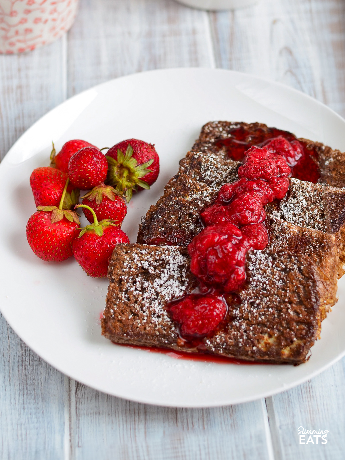 Chocolate French toast with strawberry syrup and fresh strawberries served on a white plate.