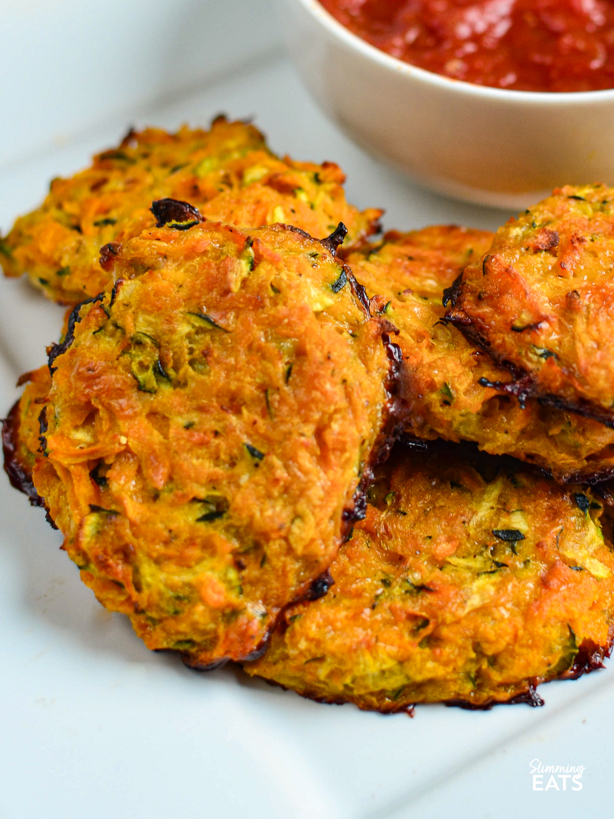 close up of Cheesy Sweet Potato and Zucchini Bites on a white plate next to a bowl of pizza sauce
