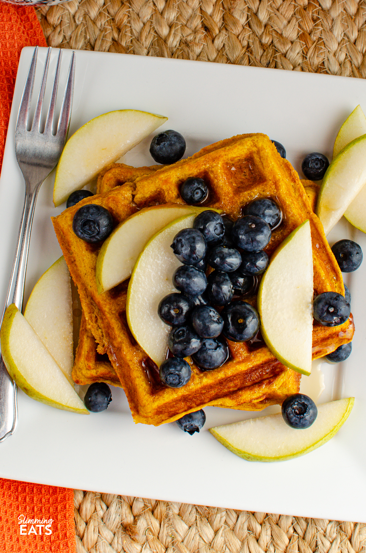 Delicious homemade oat pumpkin waffles served on a pristine white plate, adorned with fresh blueberries and slices of ripe pear, perfectly complemented by a delicate drizzle of golden maple syrup.