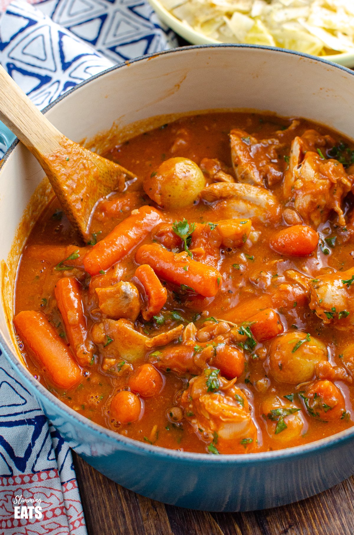 Chicken and Baked Bean Casserole - fall off the bone meat, tender pieces of chicken with delicious vegetables of carrots and new potatoes in a rich baked bean and tomato sauce. #chicken #potatoes #beans #casserole #instantpot #slowcooker #slimmingeats #weightwatchers chicken and baked bean casserole in cast iron pot with wooden spoon