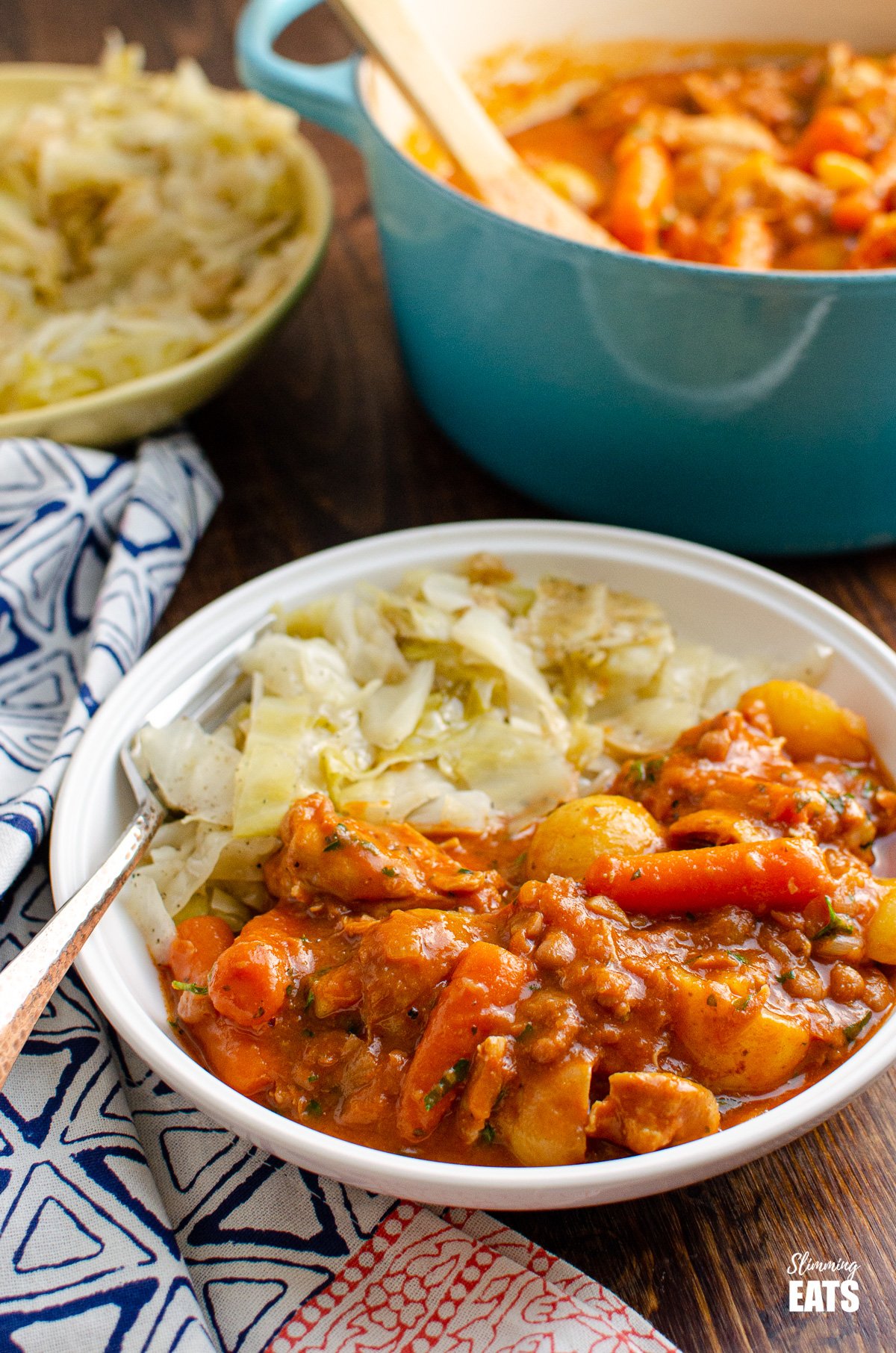 chicken and baked bean casserole in white bowl with cabbage, cast iron pot of casserole in background and bowl of cabbage