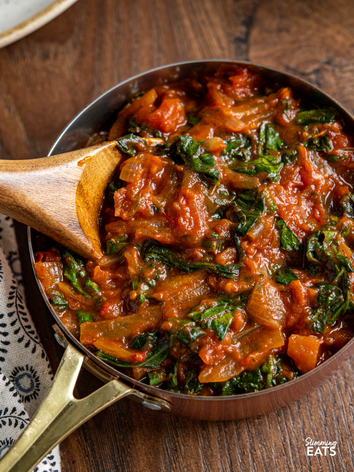 close up of balsamic tomatoes and spinach in a mini copper saucepan with wooden spoon