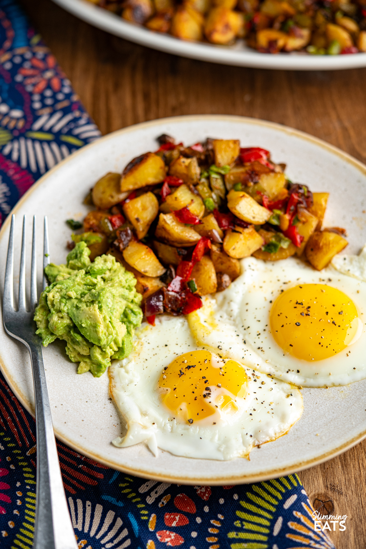 breakfast potatoes with two eggs and mashed avocado on a plate with fork. 