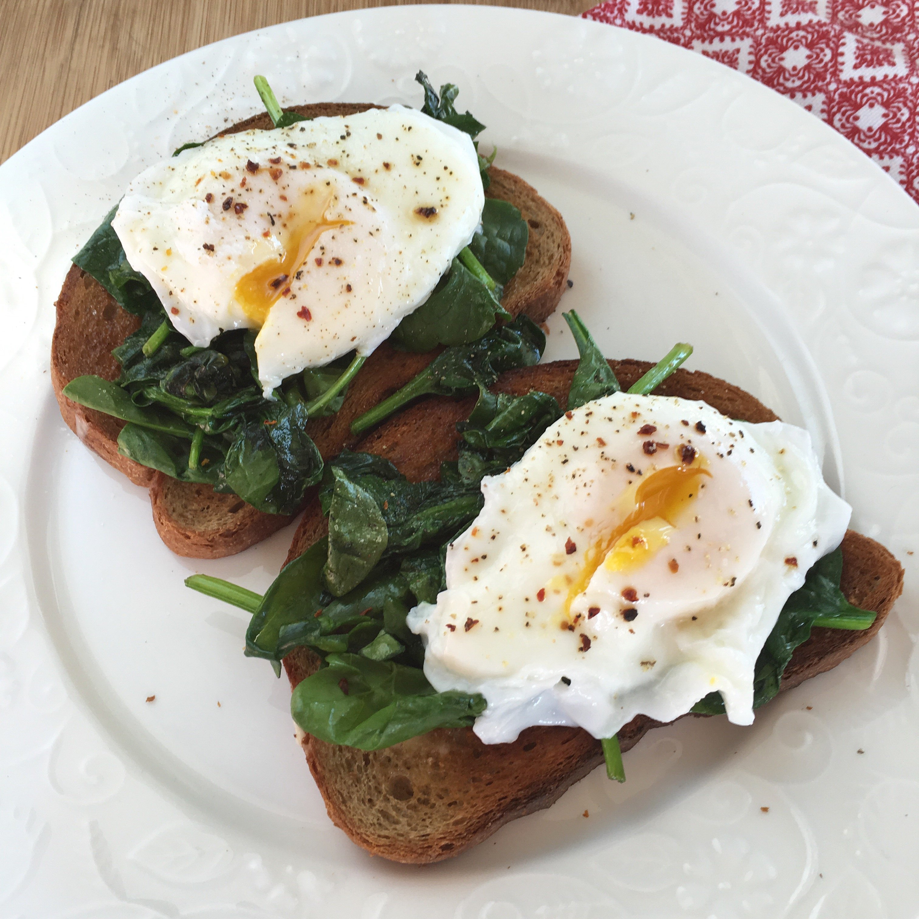 cheats poached eggs over wilted spinach and whole wheat toast on a white plate