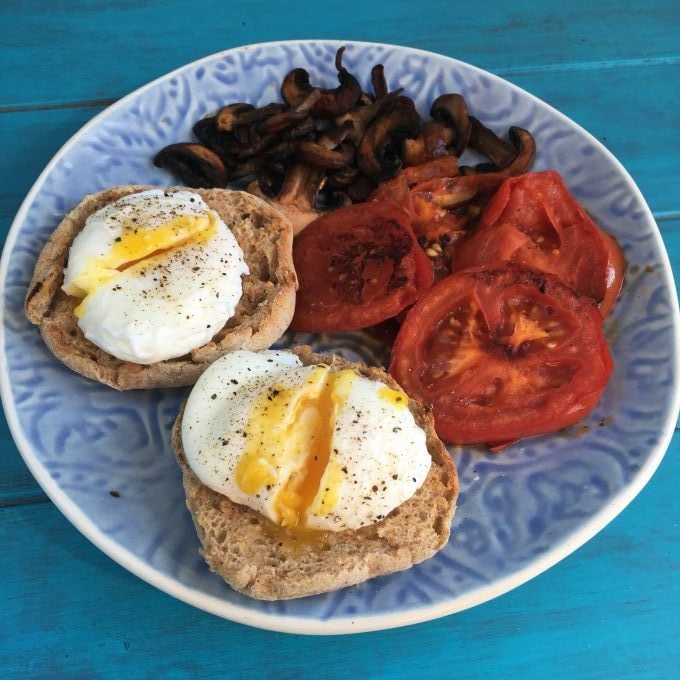 cheats poached eggs on whole wheat muffins with tomatoes and mushrooms on a blue plate