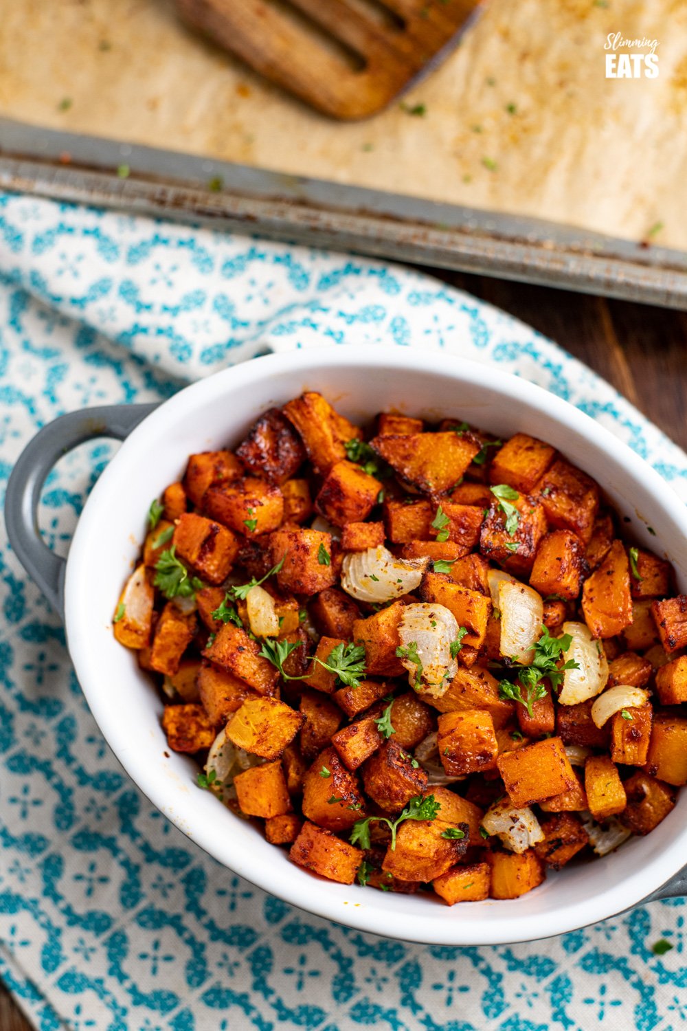 roasted butternut squash in ceramic dish on patterned napkin next to baking tray