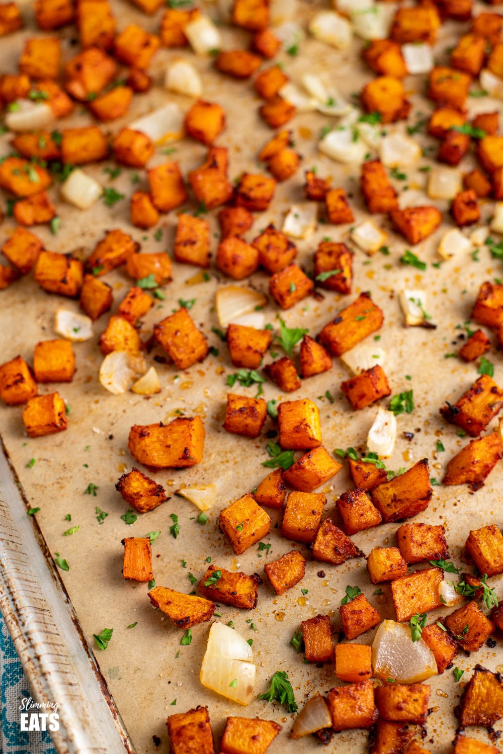 Roasted Butternut Squash with Paprika - delicious cubes of roasted butternut squash with onion, slightly caramelized on the outside and the perfect side for breakfast, lunch or dinner. Gluten Free, Dairy Free, Vegan, Paleo, Whole30, Slimming World, Weight Watchers friendly close up of seasoned roasted butternut squash on baking tray lined with parchment