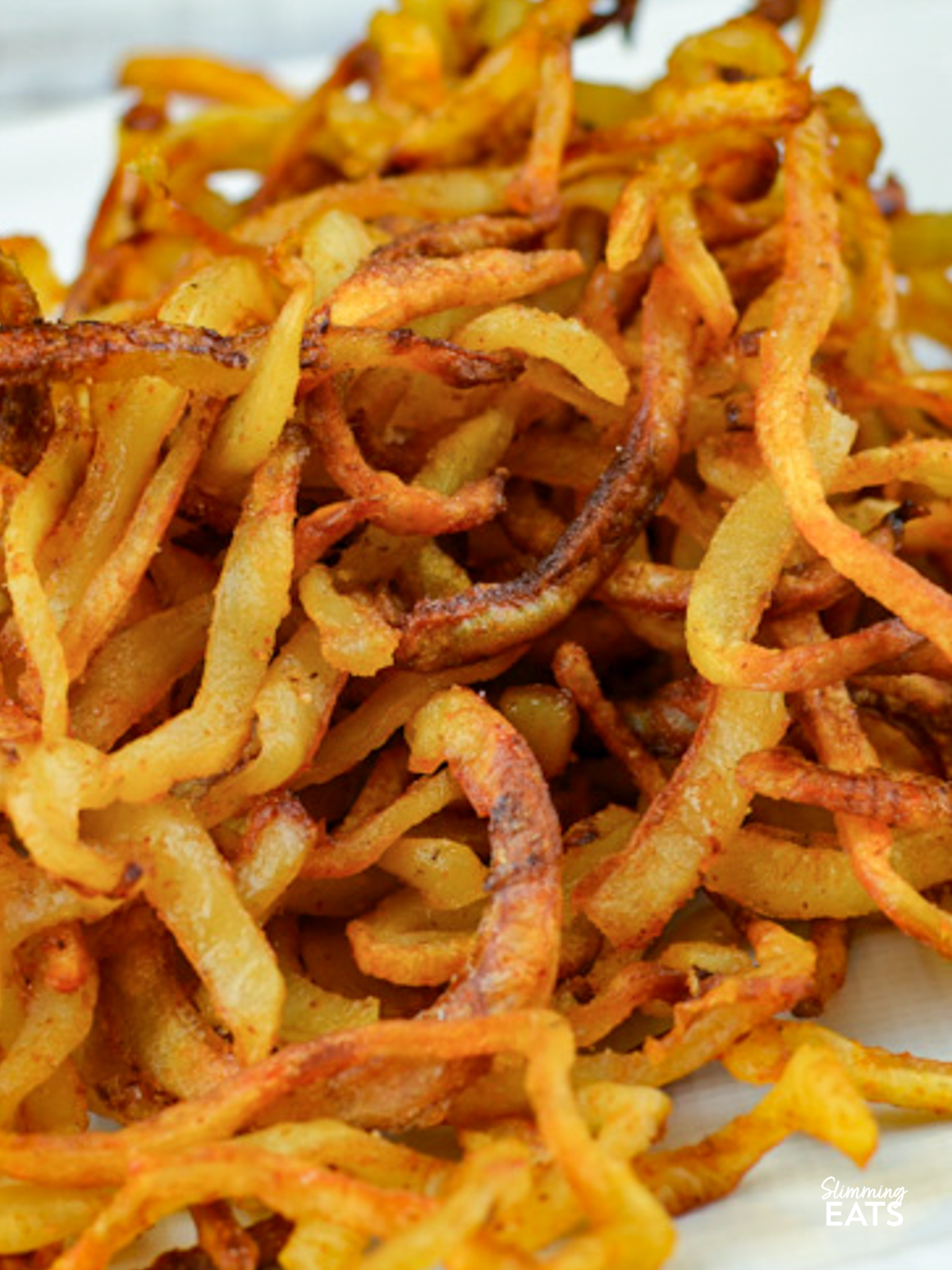 close up of seasoned curly fries on a white plate  