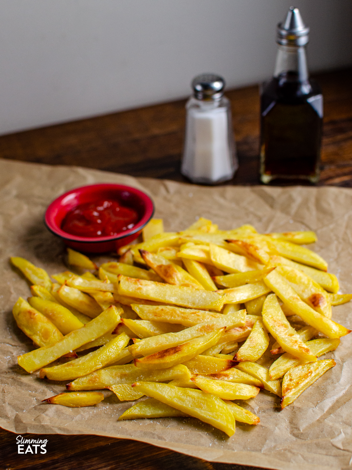 Stay on plan with my method for the PERFECT Chip Shop Chips you can make at home | gluten free, dairy free, vegan, Slimming Eats and Weight Watchers friendly Homemade Oven Baked Chip Shop Style Chips on parchment paper next to salt and vinegar and small dish with ketchup