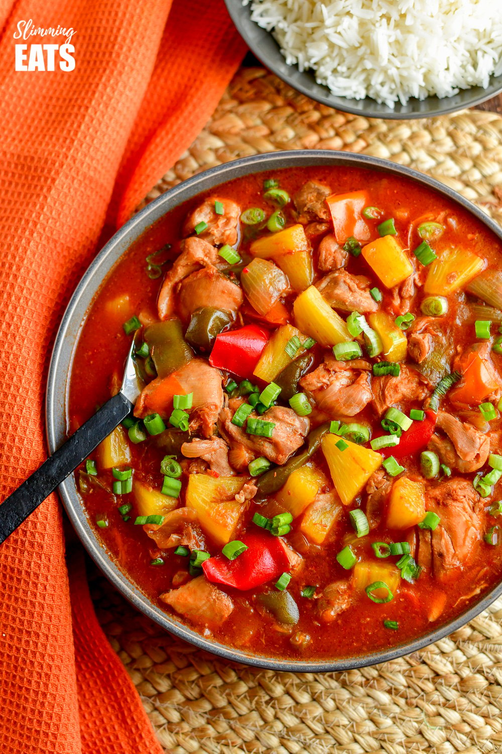 over the top view of instant pot sweet and sour chicken in grey bowl with black handled spoon.